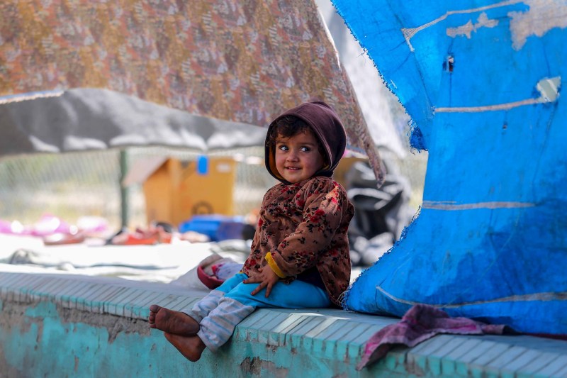 Una niña desplazada afgana sonríe bajo las lonas de la tienda en la que vive temporalmente en un parque de Kabul. Foto de EFE/ Stringer.